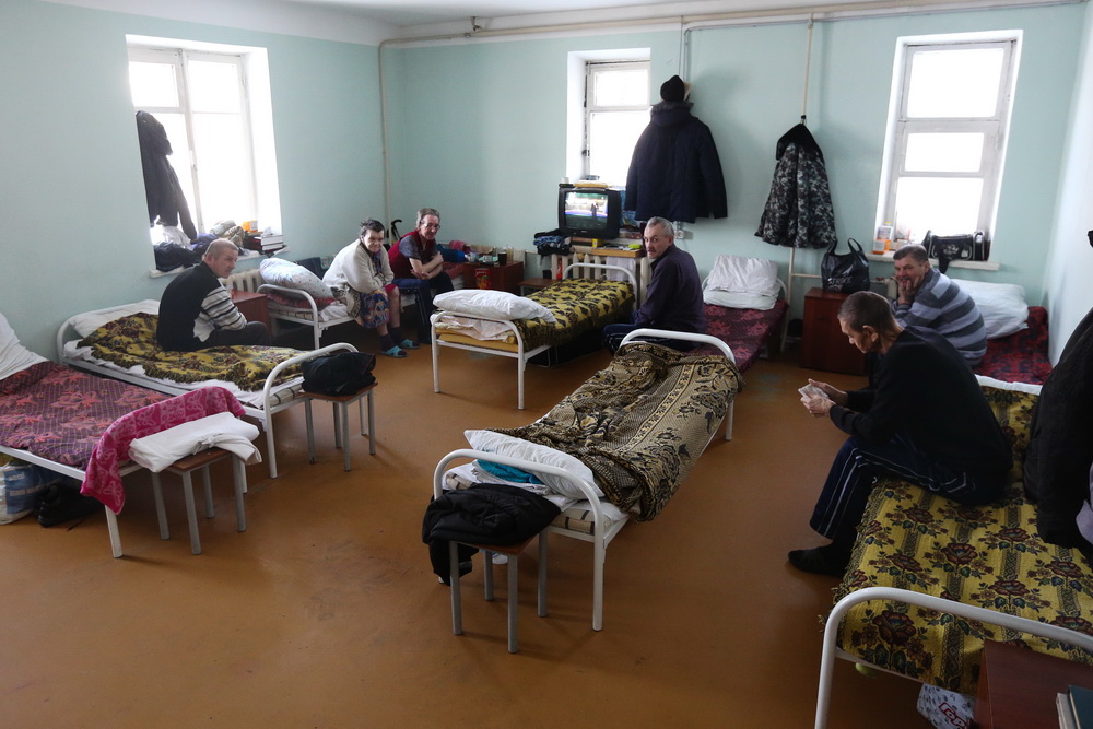 Комната с телевизором пока что больше напоминает зал ожидания. Кажется, что сидящие тут люди кого-то ждут. Чтобы не загораживать друг другу экран — рассаживаются скромно, по стеночкам.